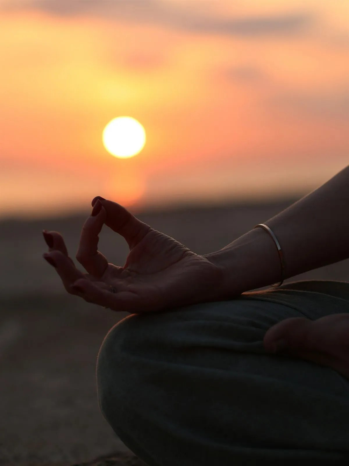 A hand resting in a meditation mudra against the setting sun